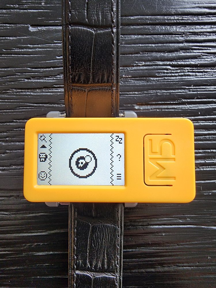 A top-down photo of the M5CStick device on a watch strap running Apocketlypse